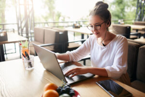 Businesswoman working remotely at cafe with headset and laptop. Mixed race female performing business negotiations on conference video chat. Telecommuting concept. Freelancer speaking on cellphone via headset.